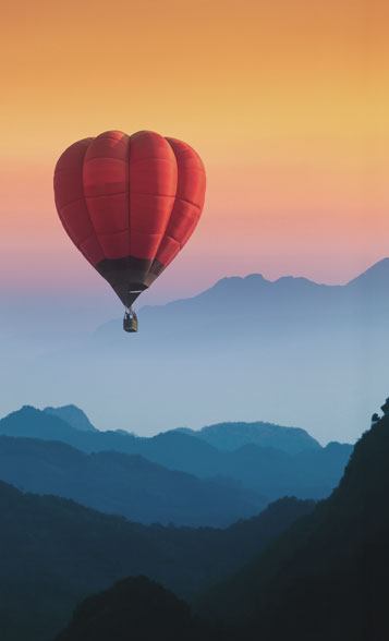 Luftbestattung, fliegender Heißluftballon, Gebirge, rötlicher Himmel